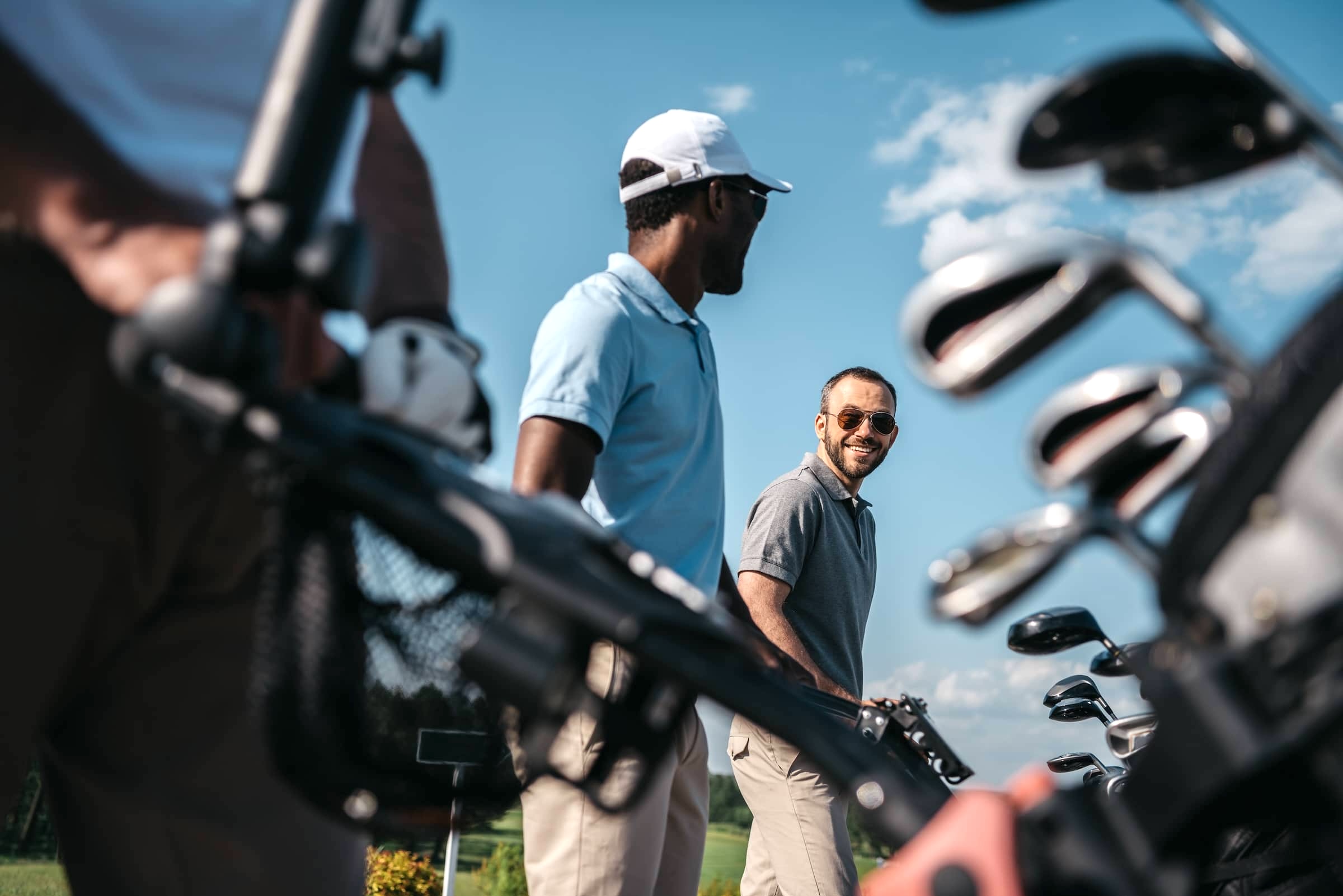 Smiling-players-going-to-the-golf-course-bag-with-clubs-at-foreground