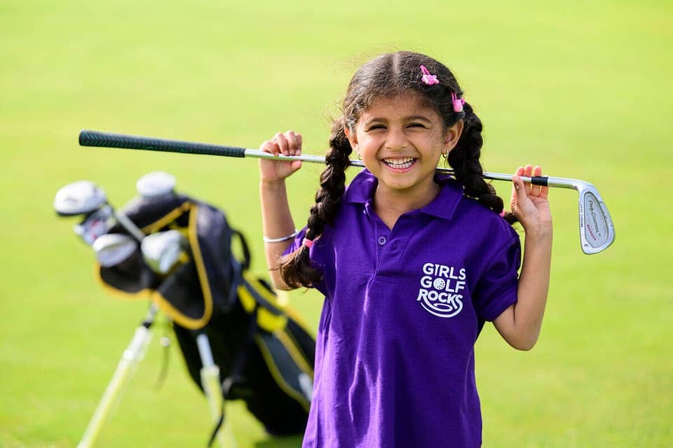 Young child smiles with golf club behind their head