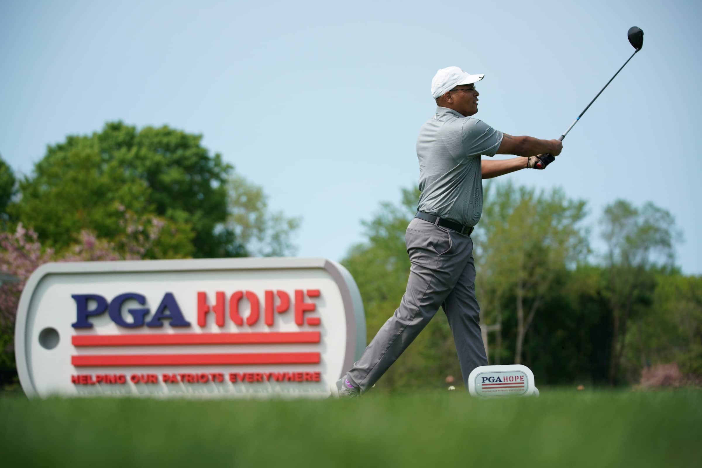Golfer tees off next to PGA HOPE advertising board