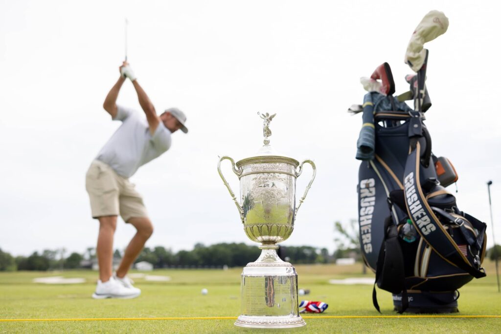 The US Open Championship Trophy is seen as Captain Bryson DeChambeau of Crushers GC hits his shot on the driving range